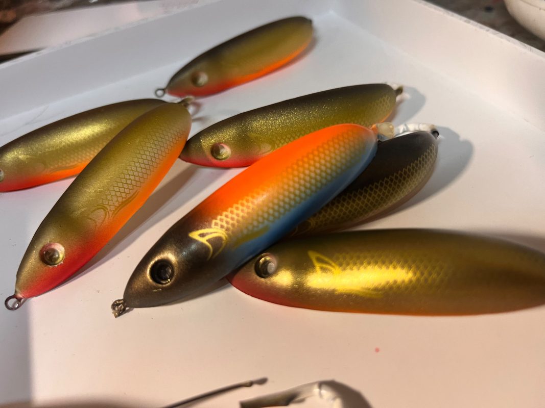 Workshop racks with hanging airbrushed lures in orange, green and blue-yellow colours