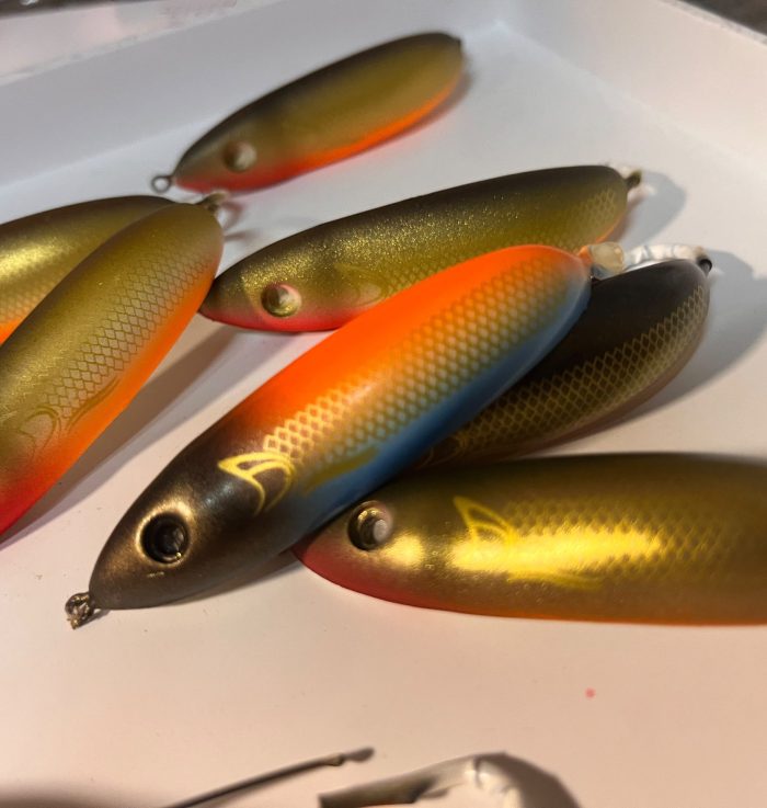 Workshop racks with hanging airbrushed lures in orange, green and blue-yellow colours